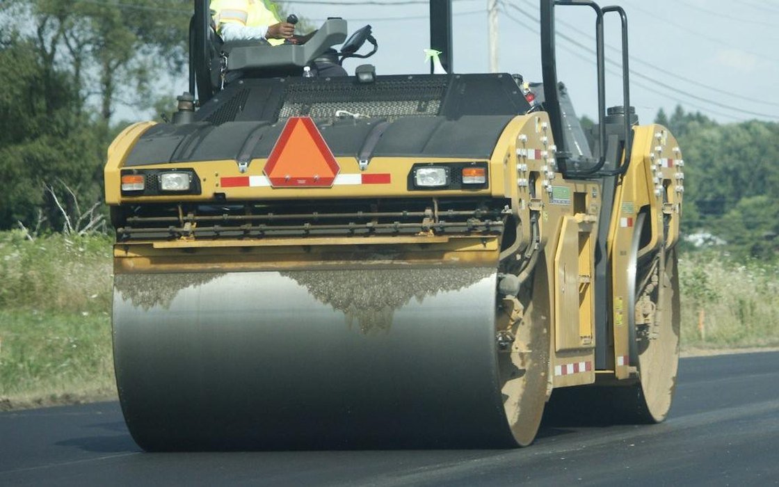 A tandem road roller compacting a freshly laid black asphalt surface on a carriageway