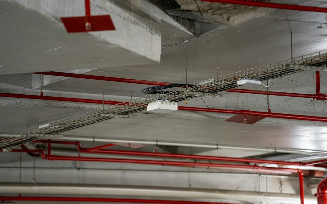 A concrete soffit carrying cable trays, red services pipework and a surface mounted light fitting