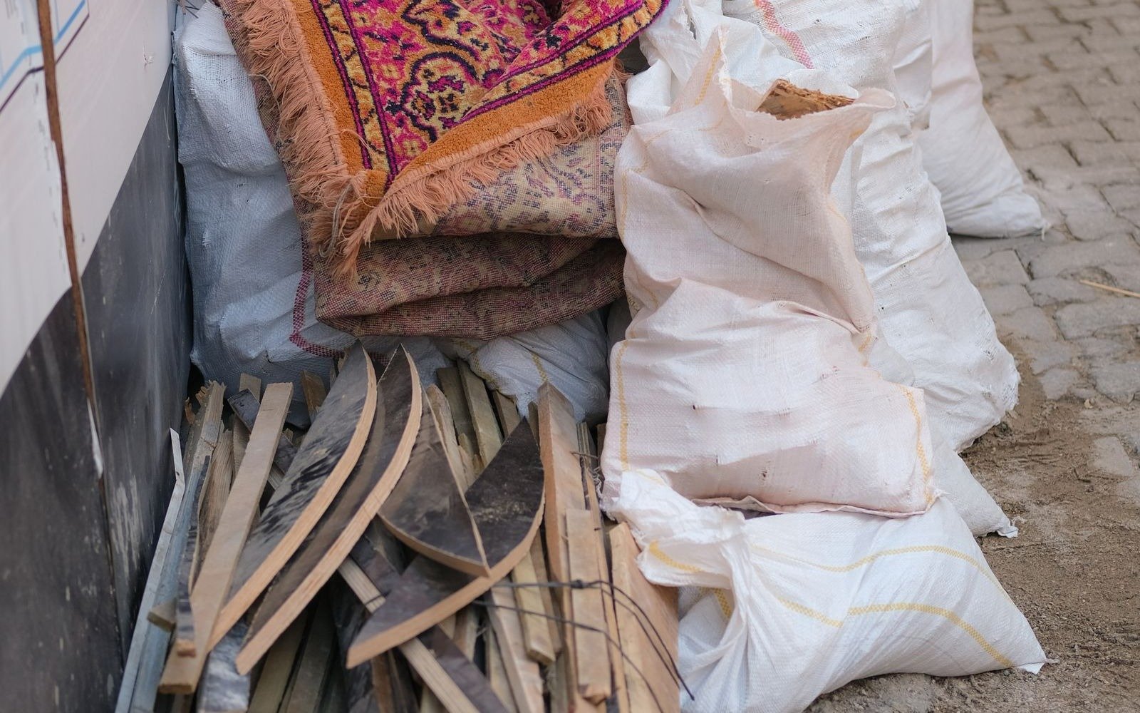 Split rubble sacks, broken timber and a discarded carpet piled against a wall at the edge of a street