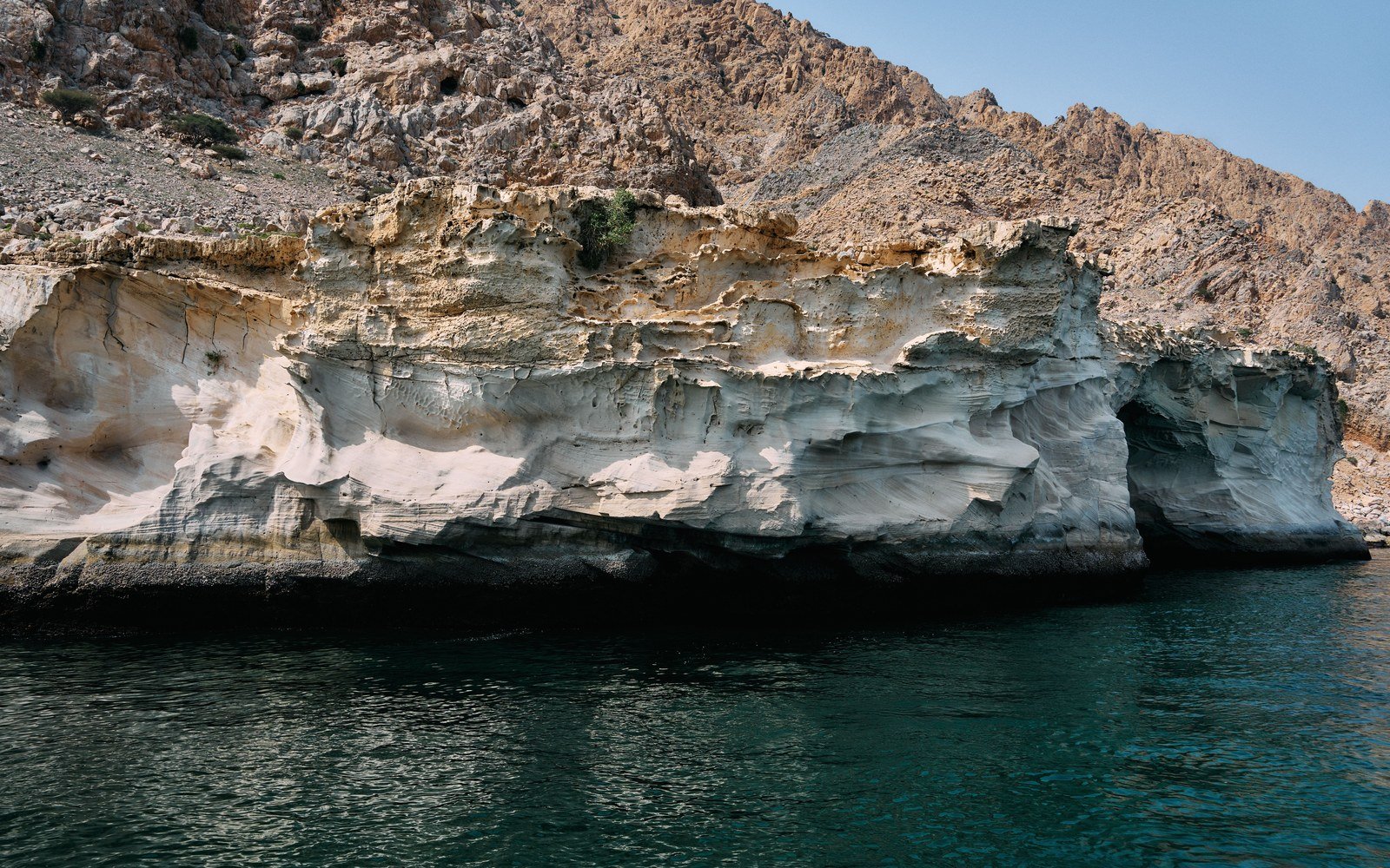 Rock cliffs falling into clear water along the Musandam coastline in Oman