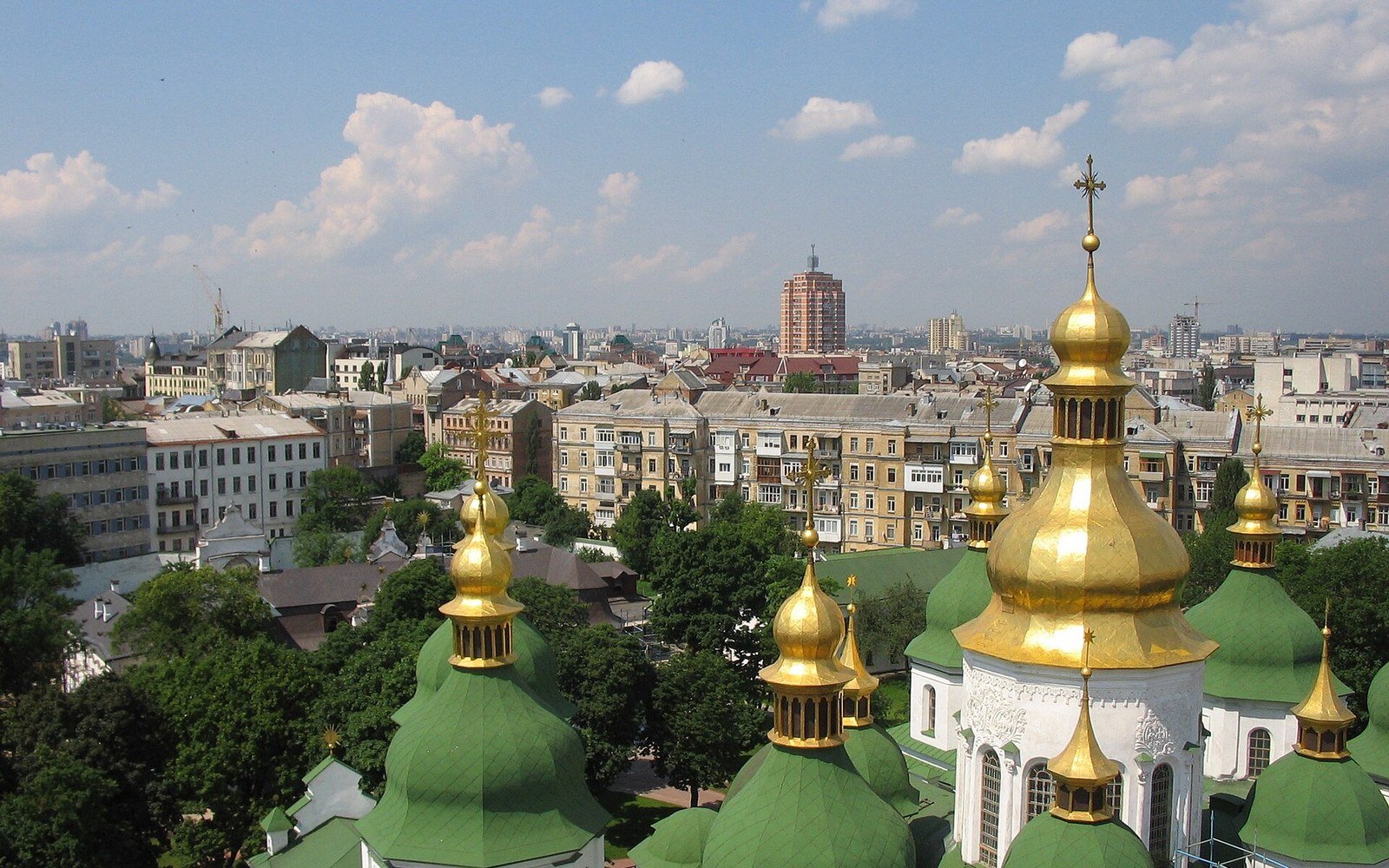 A view over the rooftops of Kyiv on a clear day, with green domes and gilded cupolas in the foreground and the blocks, streets and trees of the city running away to the horizon