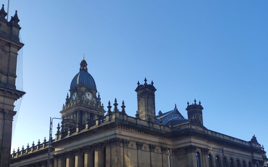 The domed clock tower and stone colonnade of Leeds Town Hall against a clear blue sky