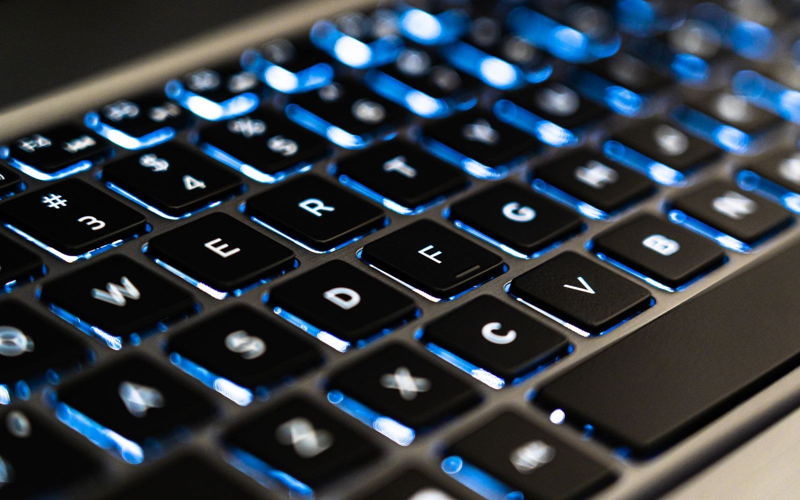 Backlit laptop keyboard in low light with blue illuminated keys