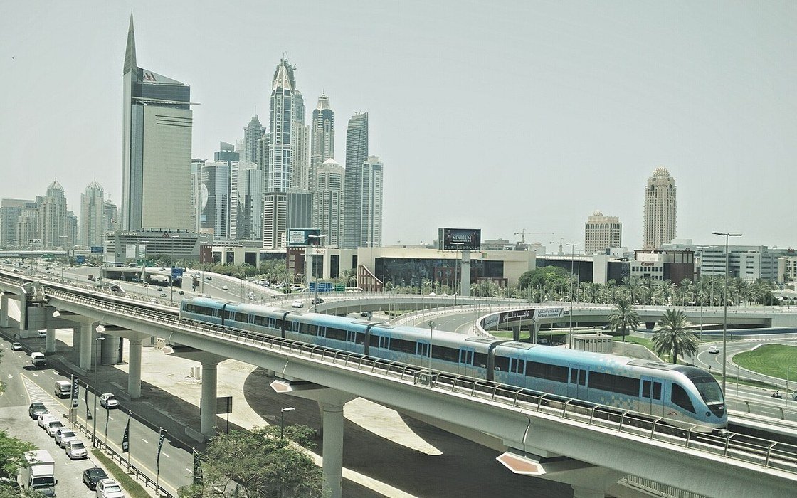 A Dubai skyline in daylight with a metro train crossing the elevated viaduct