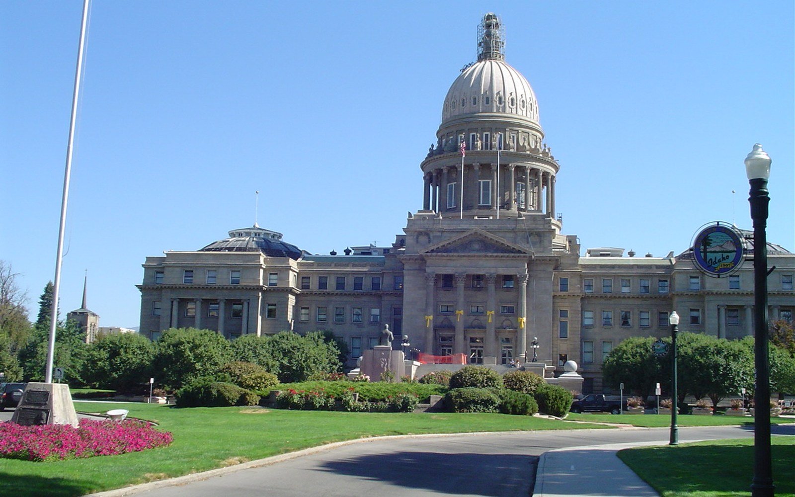 The Idaho State Capitol in Boise seen from the south lawn on a clear day, its sandstone dome above a columned portico, with mown grass, flower beds and clipped shrubs in the foreground