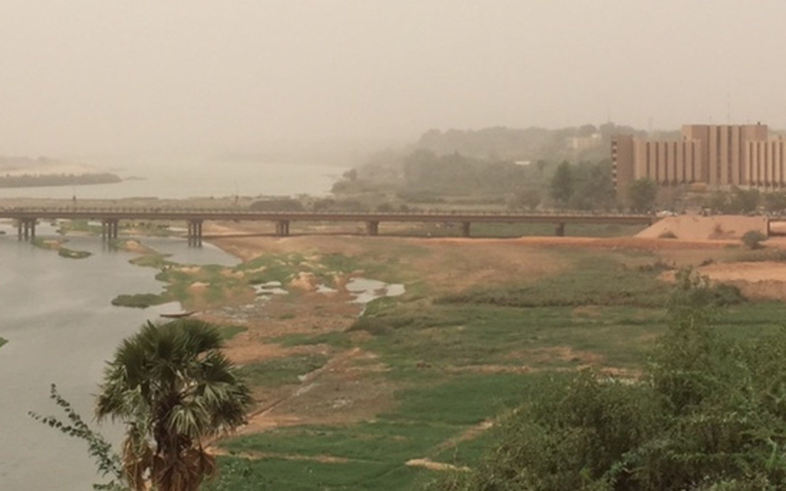 A road bridge crossing the Niger river at Niamey with the city behind it in dust haze