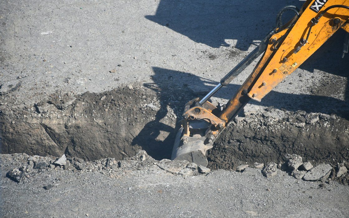 An excavator bucket cutting a narrow trench through a road surface