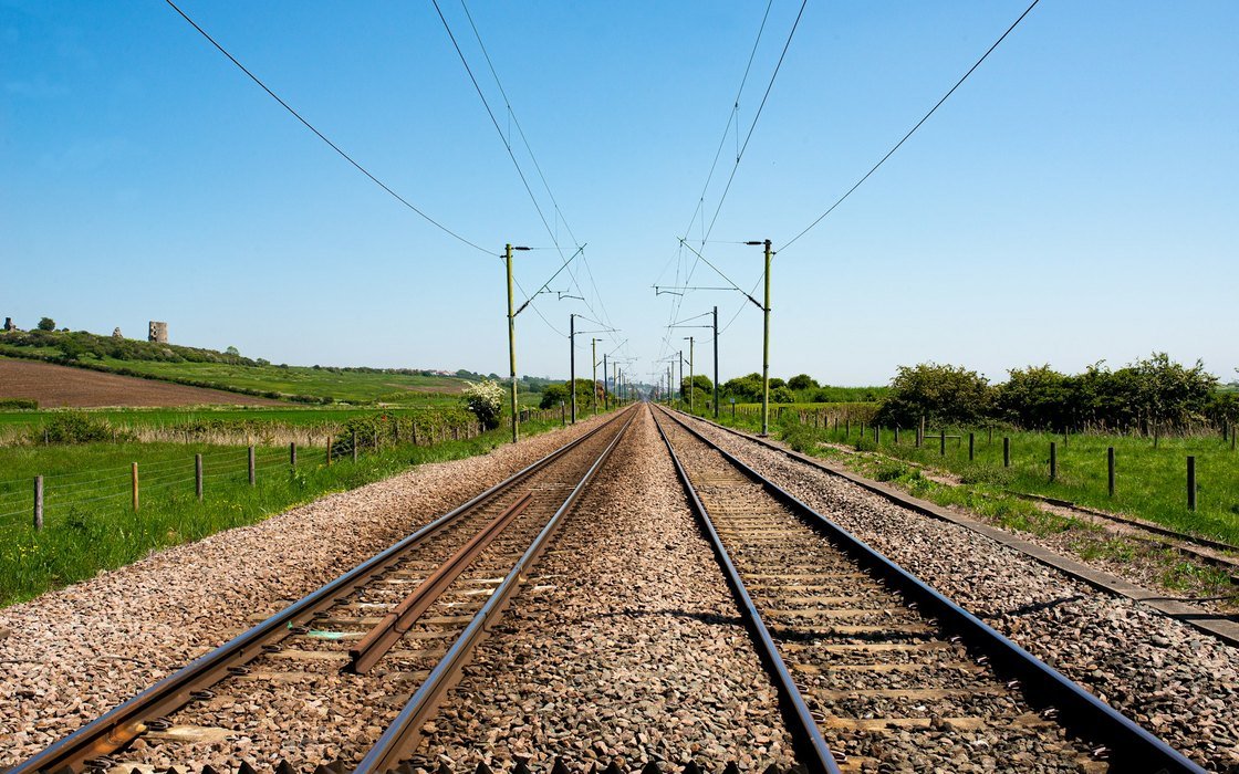 Two railway tracks running away from the camera between grass verges under overhead line equipment