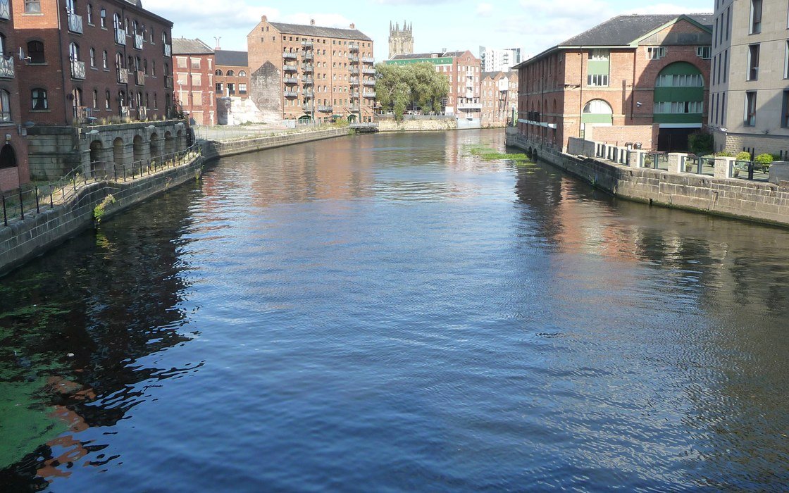 The River Aire running between converted brick warehouses and modern riverside blocks in central Leeds on a clear day