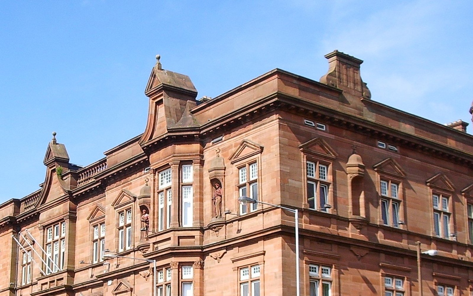 The upper storeys and corner turret of a red sandstone municipal building against a clear sky