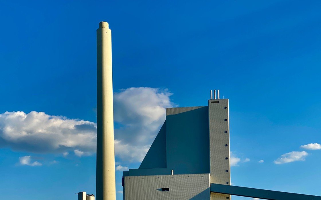 A thermal treatment plant with a tall exhaust stack and clad process building against a clear sky