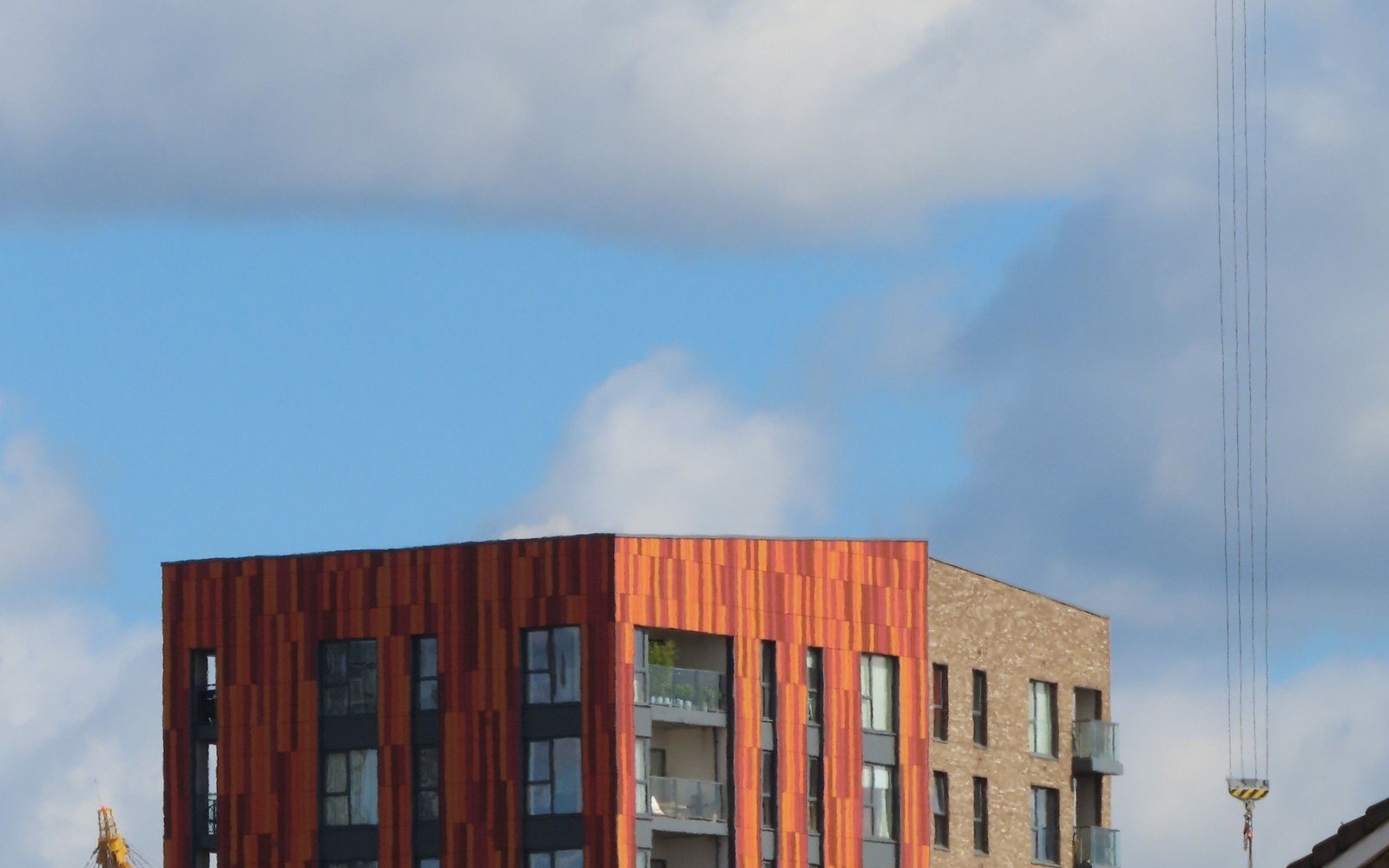 A contemporary residential block clad in timber coloured panels and pale brick, photographed from below against a partly clouded sky