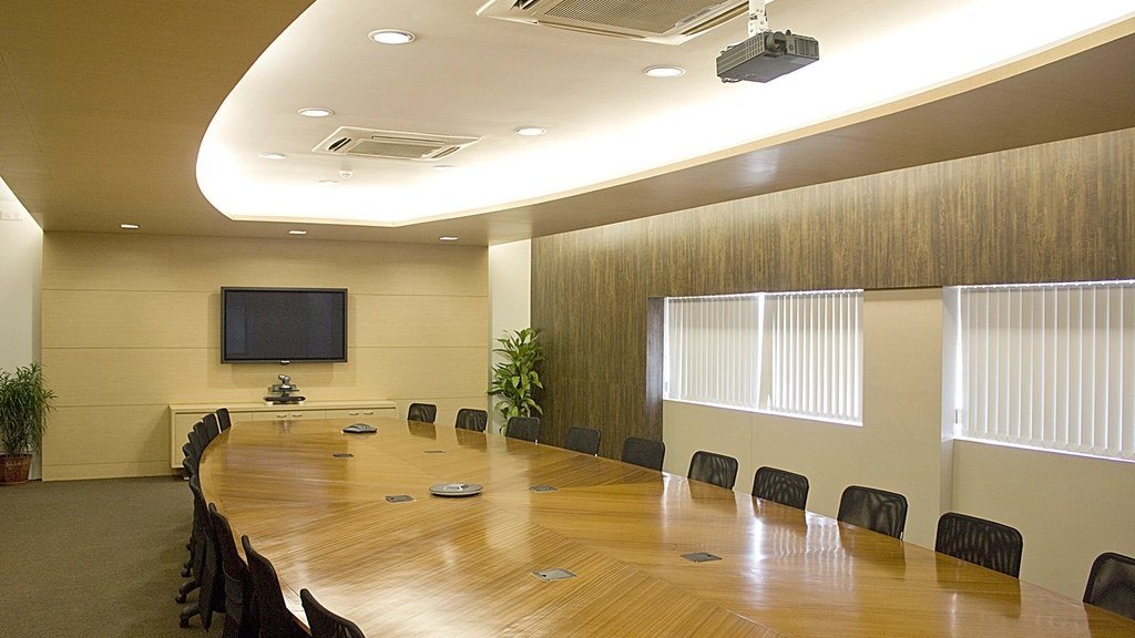 An empty boardroom with a long table, ranked chairs and a wall screen