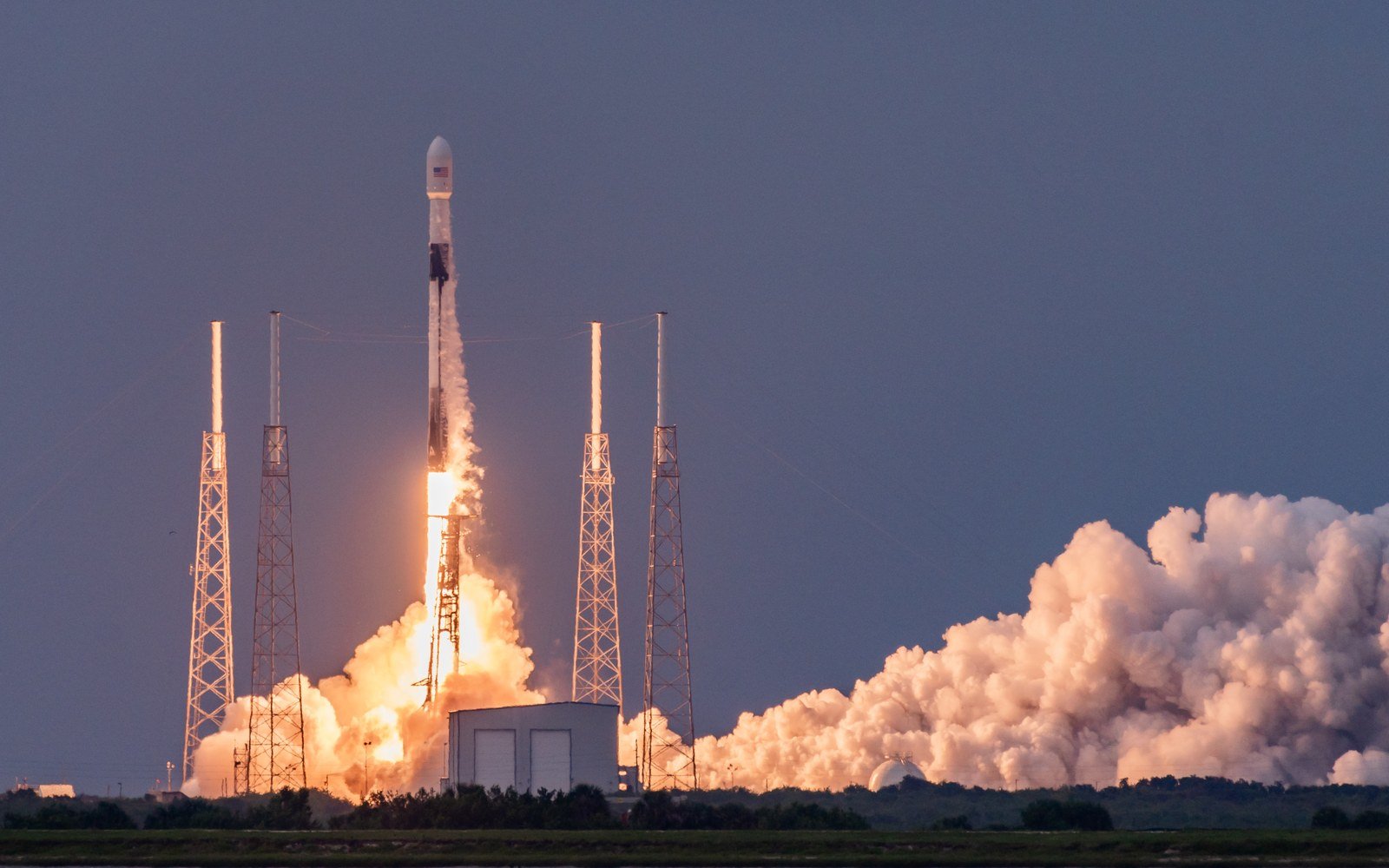 A rocket climbing away from a coastal launch pad on a column of exhaust under a clear sky