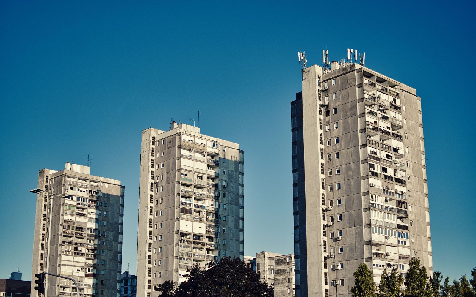 A group of tall concrete residential tower blocks against a clear blue sky