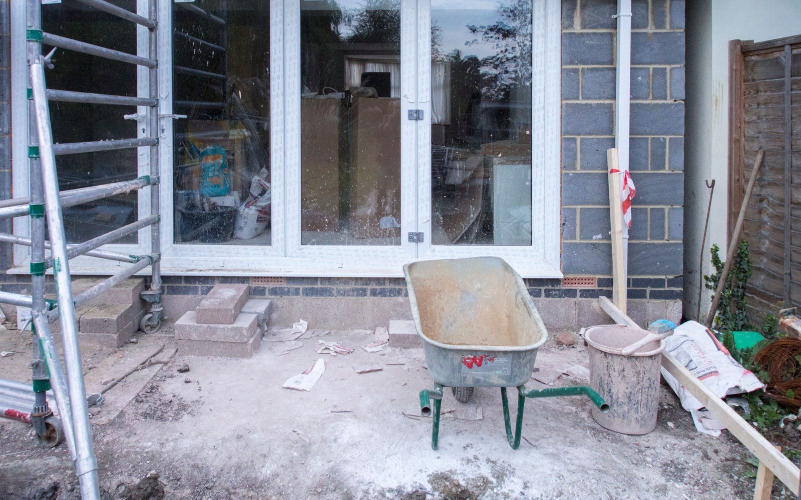 A rear extension part built behind a house, blockwork up to first floor level, a mobile tower, a wheelbarrow and a mixing tub on bare screed