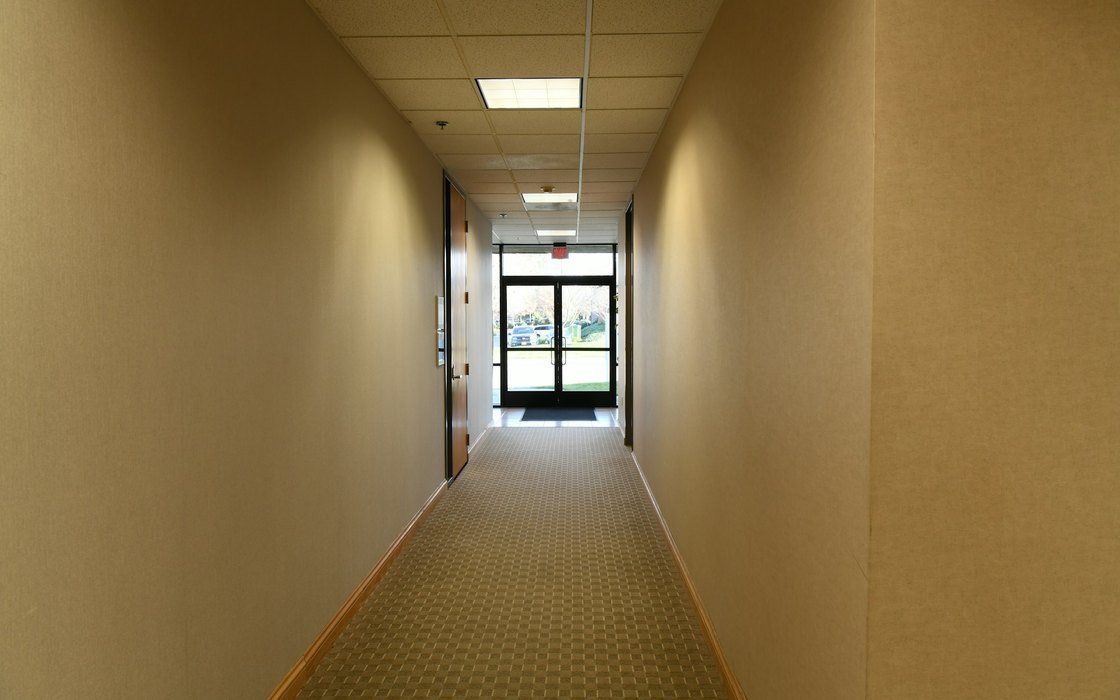 An empty building corridor with a timber doorset on one side and glazed doors at the far end