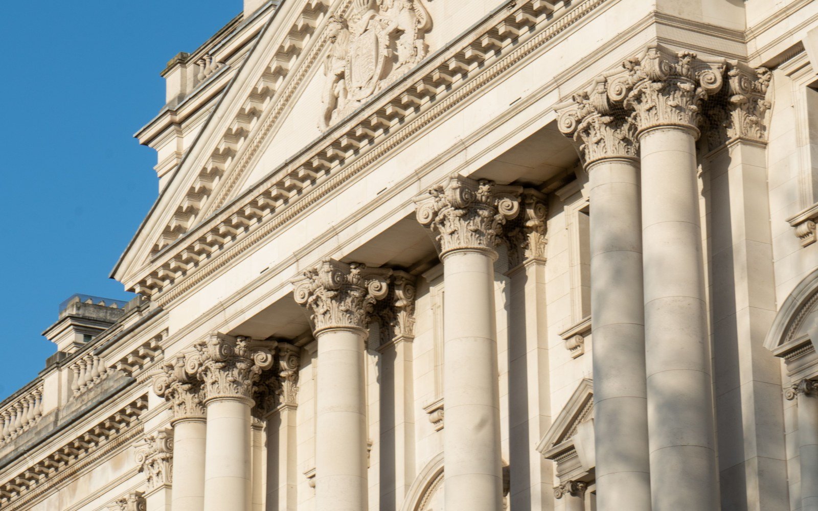 The Corinthian colonnade and pediment of a classical government building in Portland stone, photographed from the pavement against a clear sky