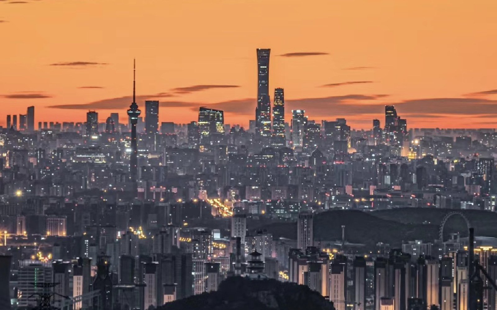 A city skyline at dusk with tall towers standing against an orange sky