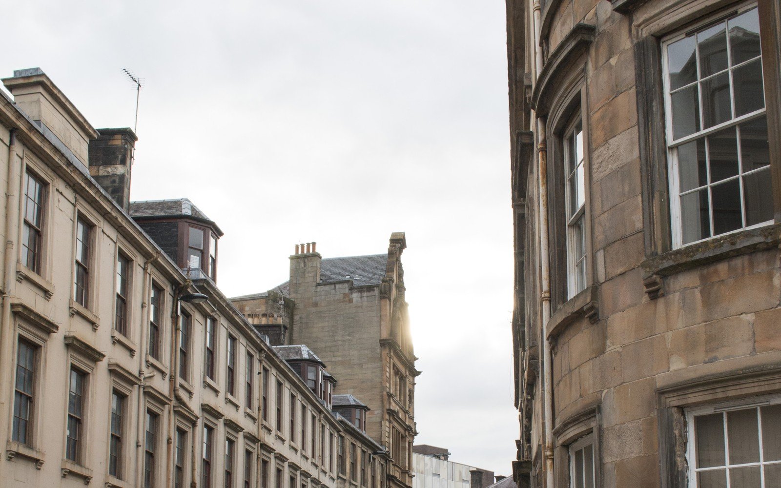 A curving terrace of sandstone tenement buildings with sash windows and stone bay fronts