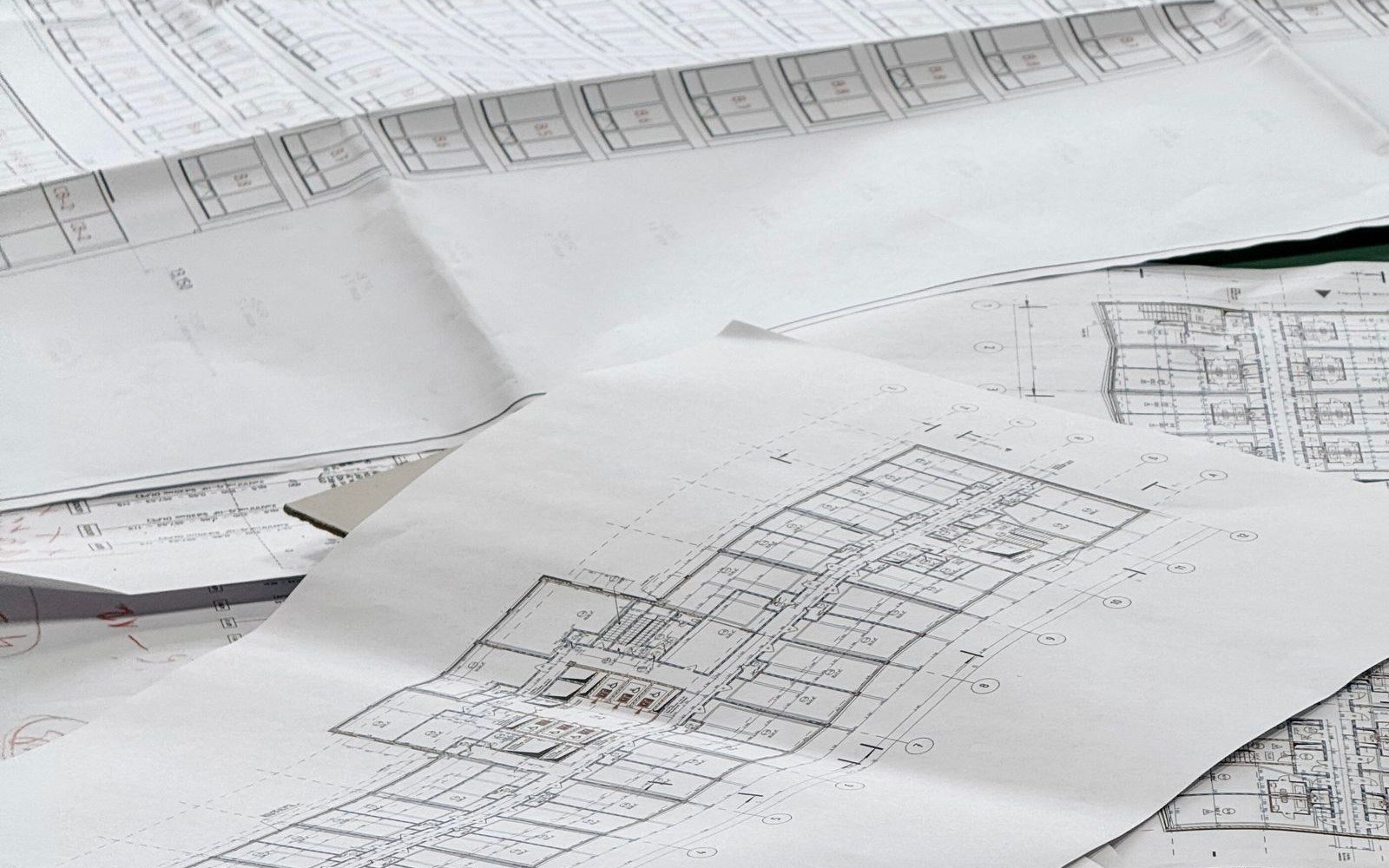 Loose sheets of technical drawings spread across a desk, with floor plans and dimension lines visible
