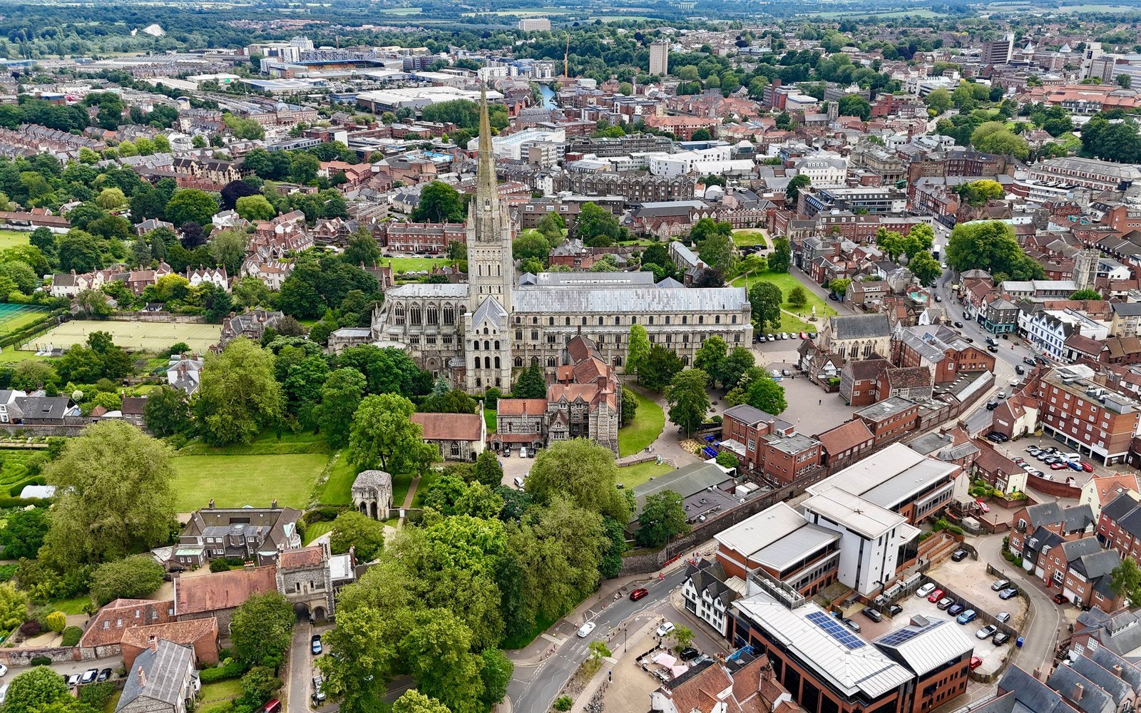 An elevated view across Norwich with the cathedral and its spire at the centre, surrounded by trees and terraces of red brick housing