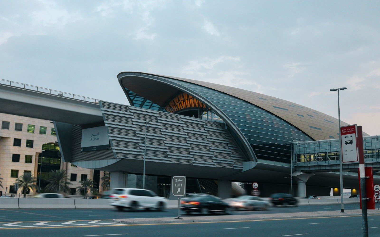 A curved metro station shell above a multi lane road, with traffic passing beneath