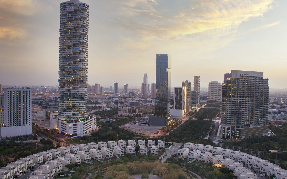 Aerial view of Dubai at dusk showing residential towers above lower housing and open ground