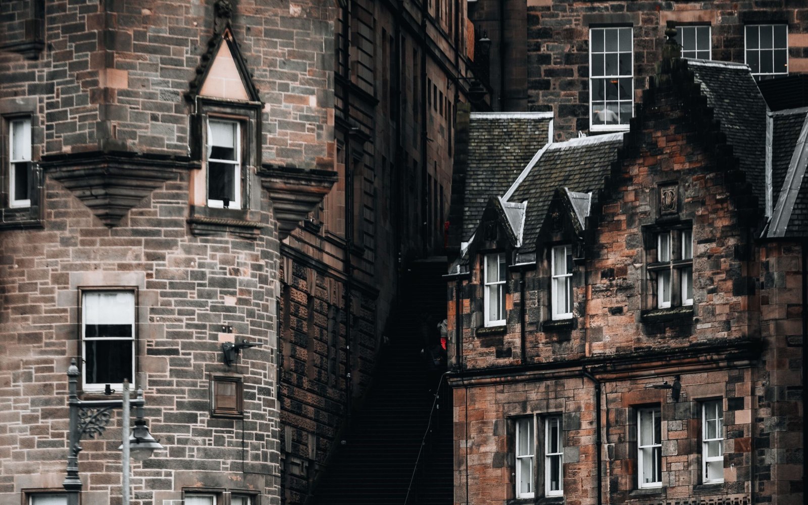 Stone tenement buildings with dormer windows and crow stepped gables rising above a narrow street in Edinburgh