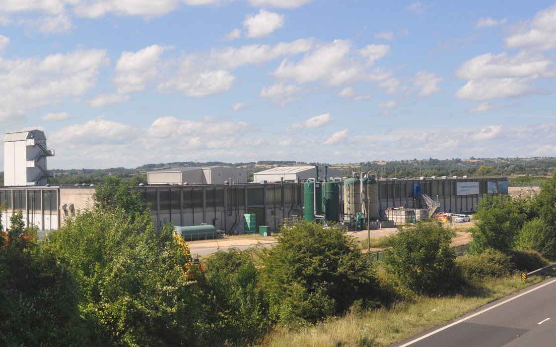 Process tanks and plant buildings of a water treatment works seen across trees from a road