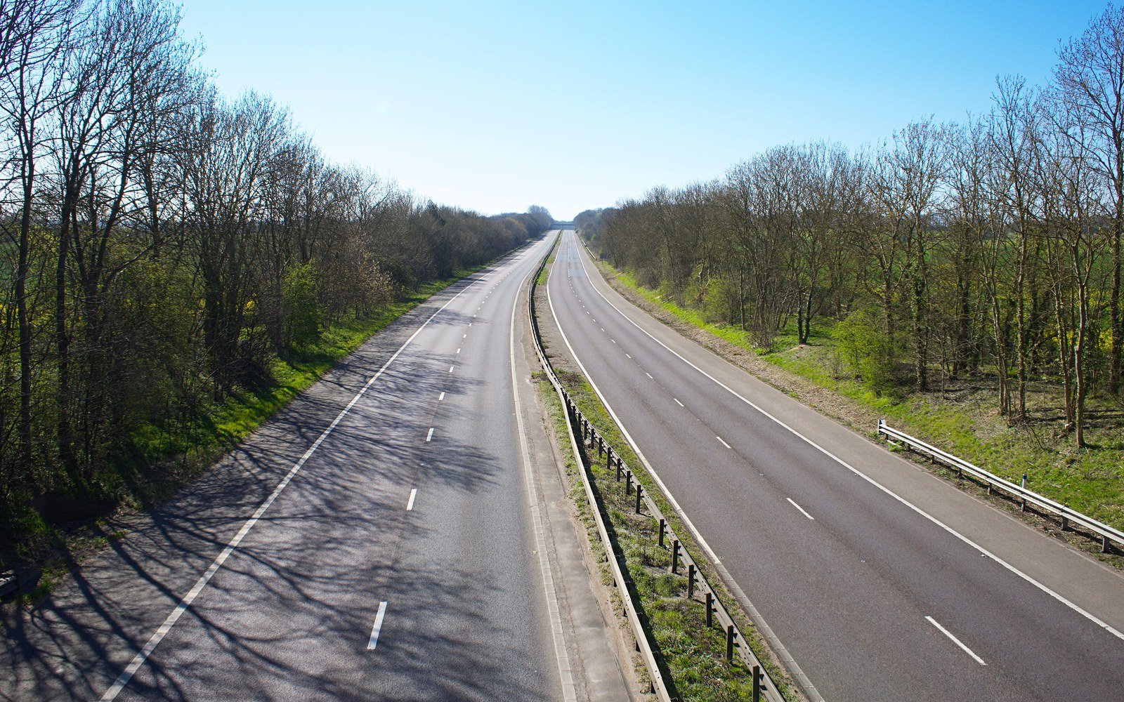 An empty dual carriageway running away to the horizon between leafless trees under a clear sky