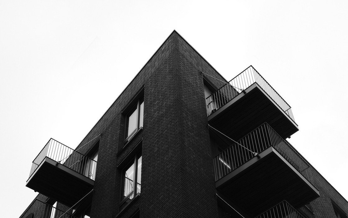 A dark brick residential block in London seen from below, with projecting balconies on each floor