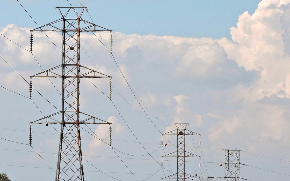 High voltage transmission towers carrying overhead lines across open ground under broken cloud