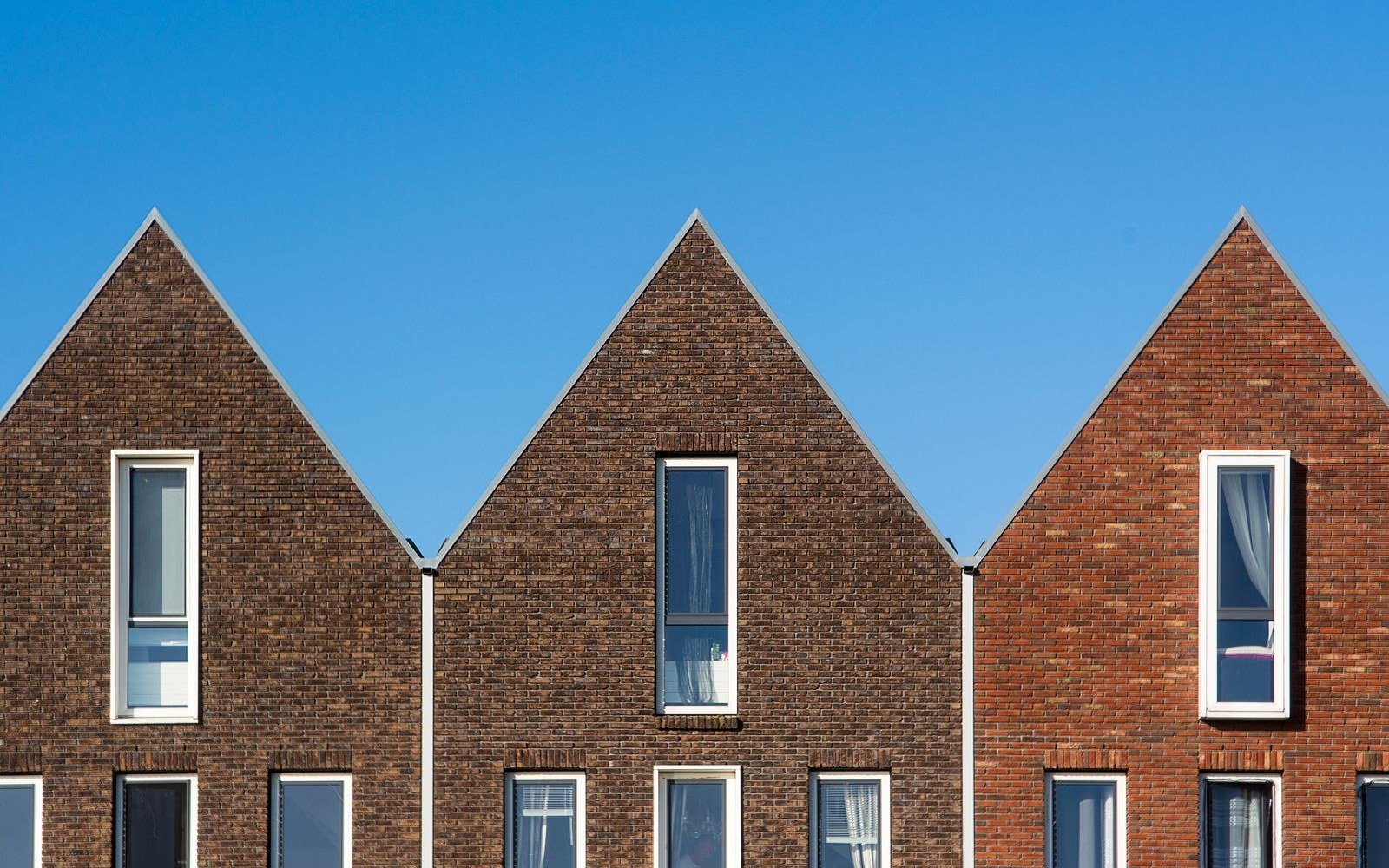 Three brick houses with steeply pitched gable ends and tall narrow windows standing against a clear blue sky