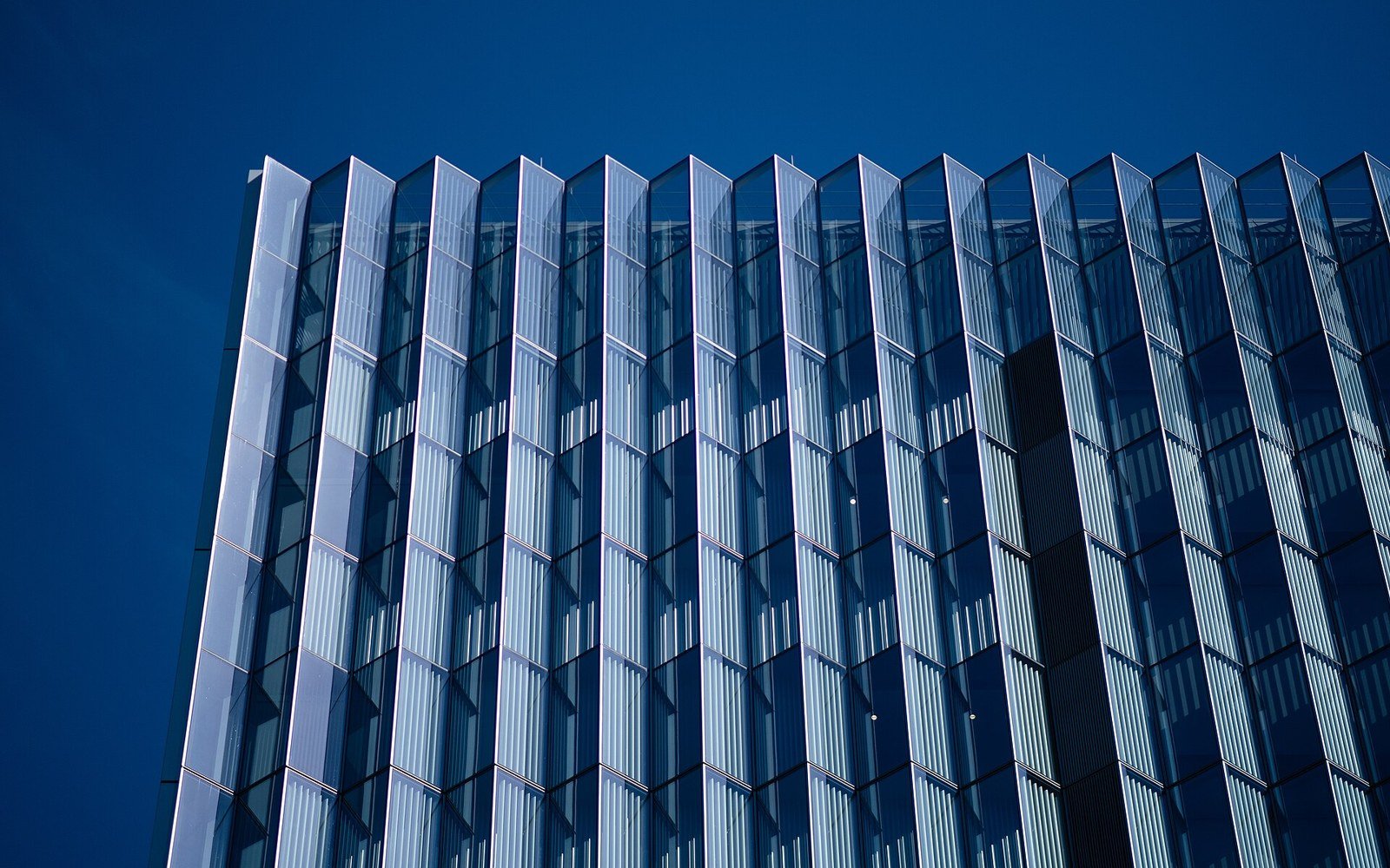 The glazed facade of a modern courthouse rising against a deep blue sky, its vertical fins casting a regular rhythm of light and shadow