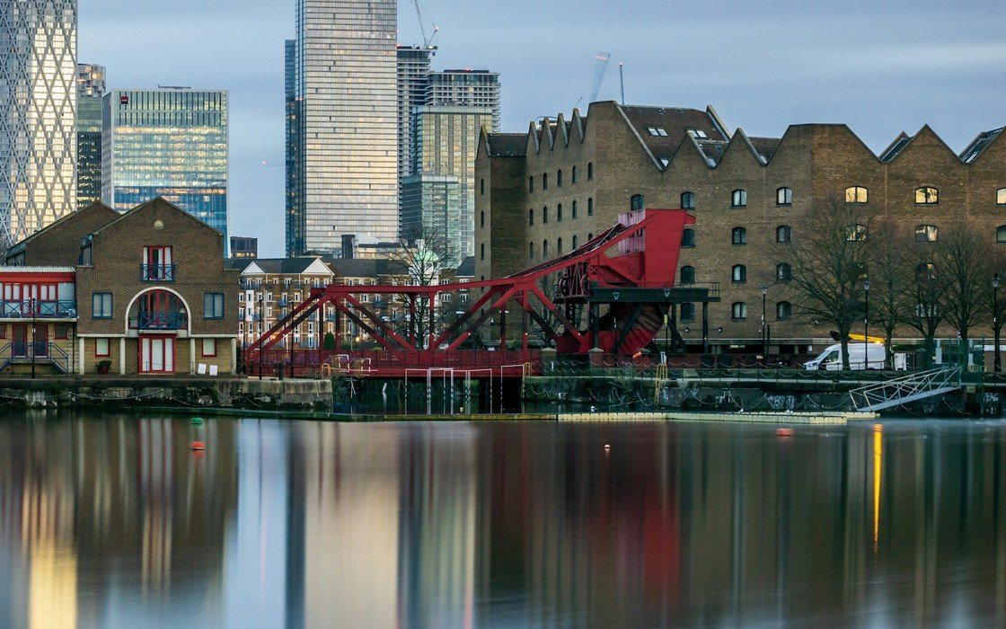 Converted dock warehouses and a red bascule bridge reflected in still water at Shadwell Basin