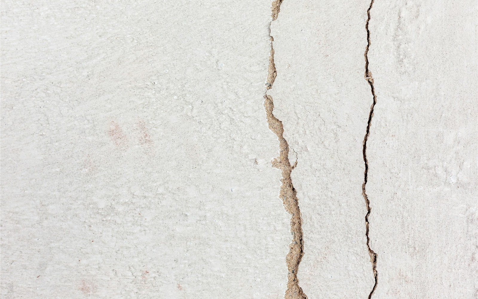 Two cracks running down a white rendered wall, one wide and stepped, the other fine and straight