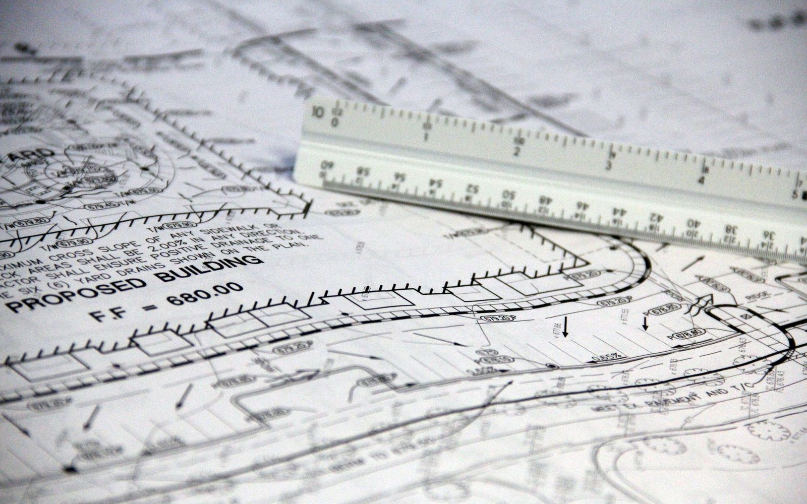 Civil engineering site drawing with levels, drainage falls and a scale rule laid across it