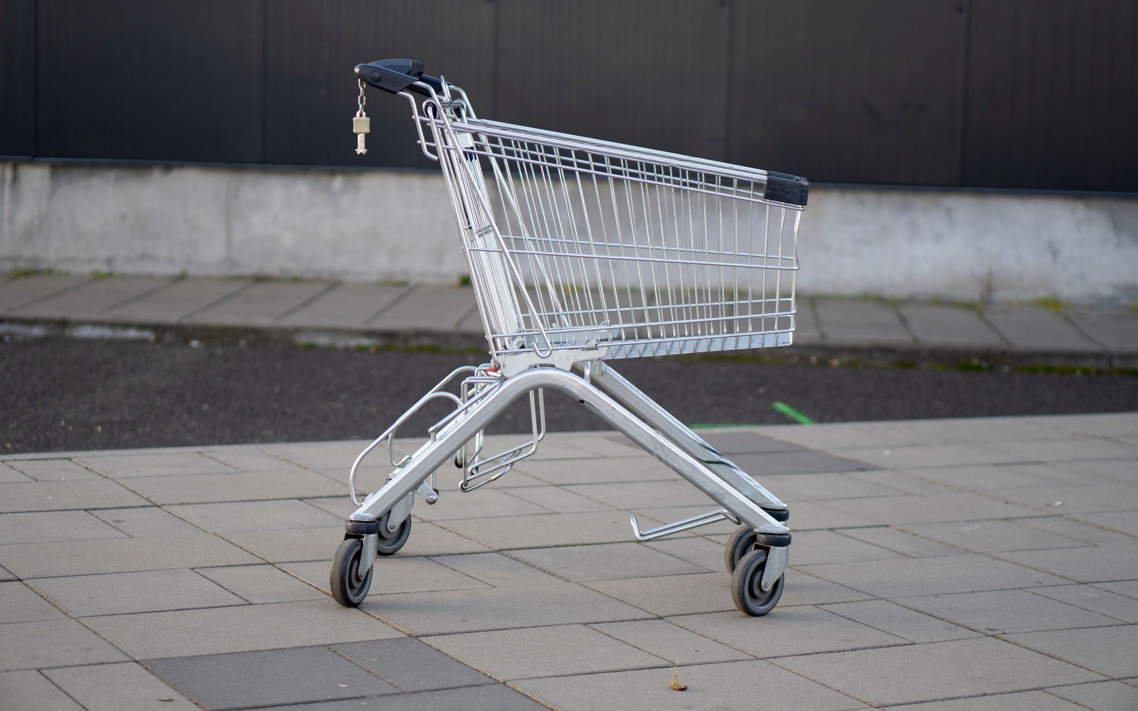 An empty shopping trolley standing on a pavement beside a plain dark wall