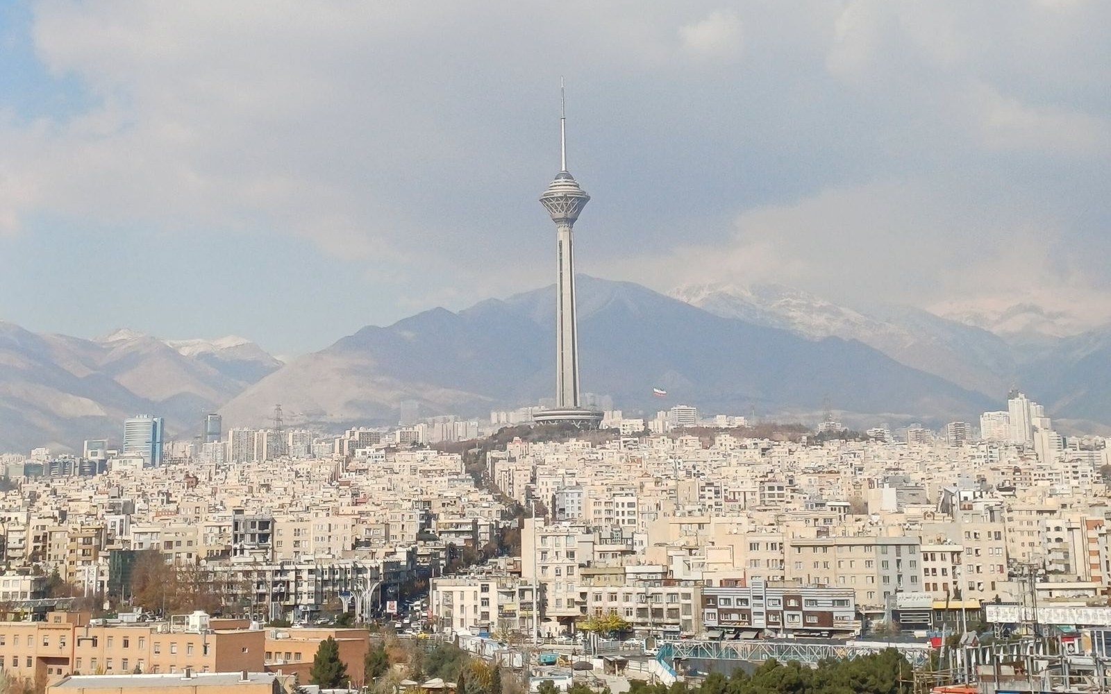 The Milad Tower rising over the rooftops of Tehran, with the snow-streaked Alborz mountains behind