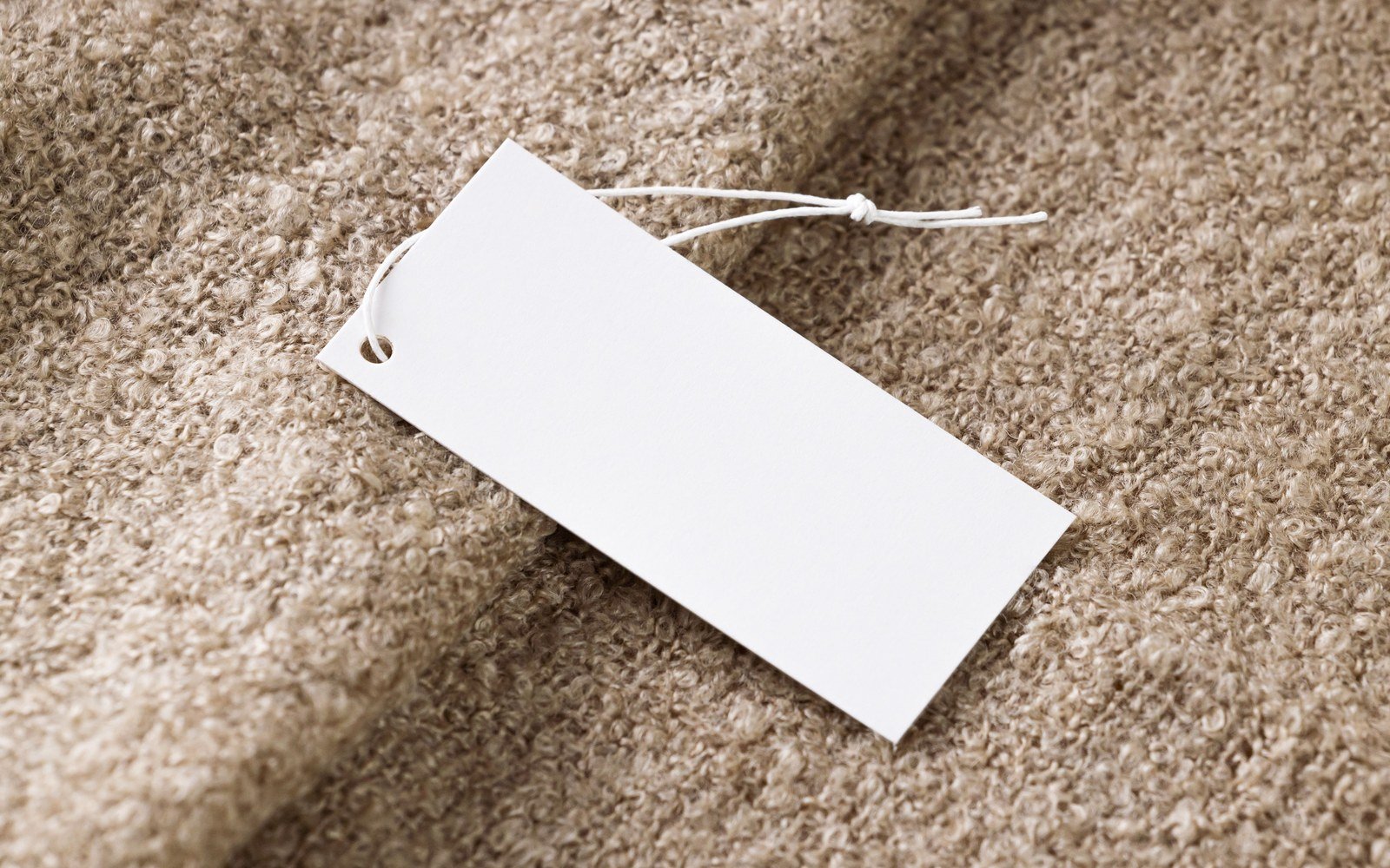 A blank white price tag with a cord tie lying on a textured beige fabric surface