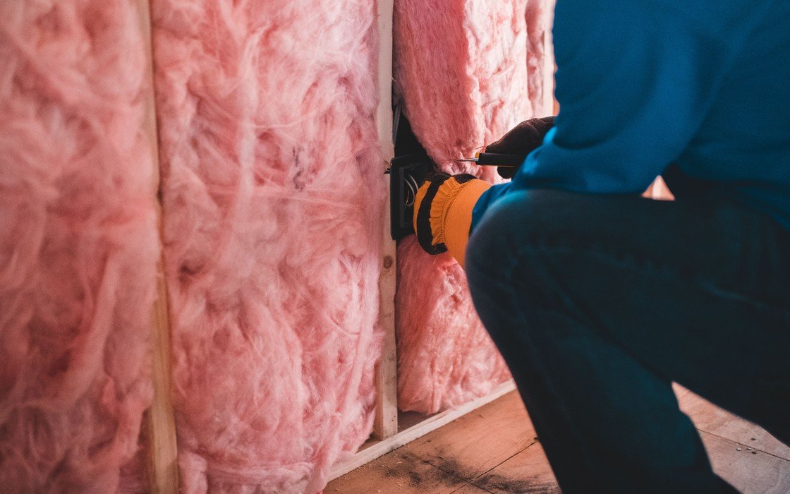 A gloved worker fitting mineral wool insulation between timber studs, the face out of frame