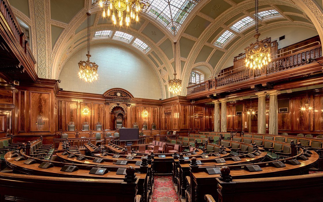 The wood panelled council chamber of Bradford City Hall, empty, with chandeliers below a glazed barrel vault