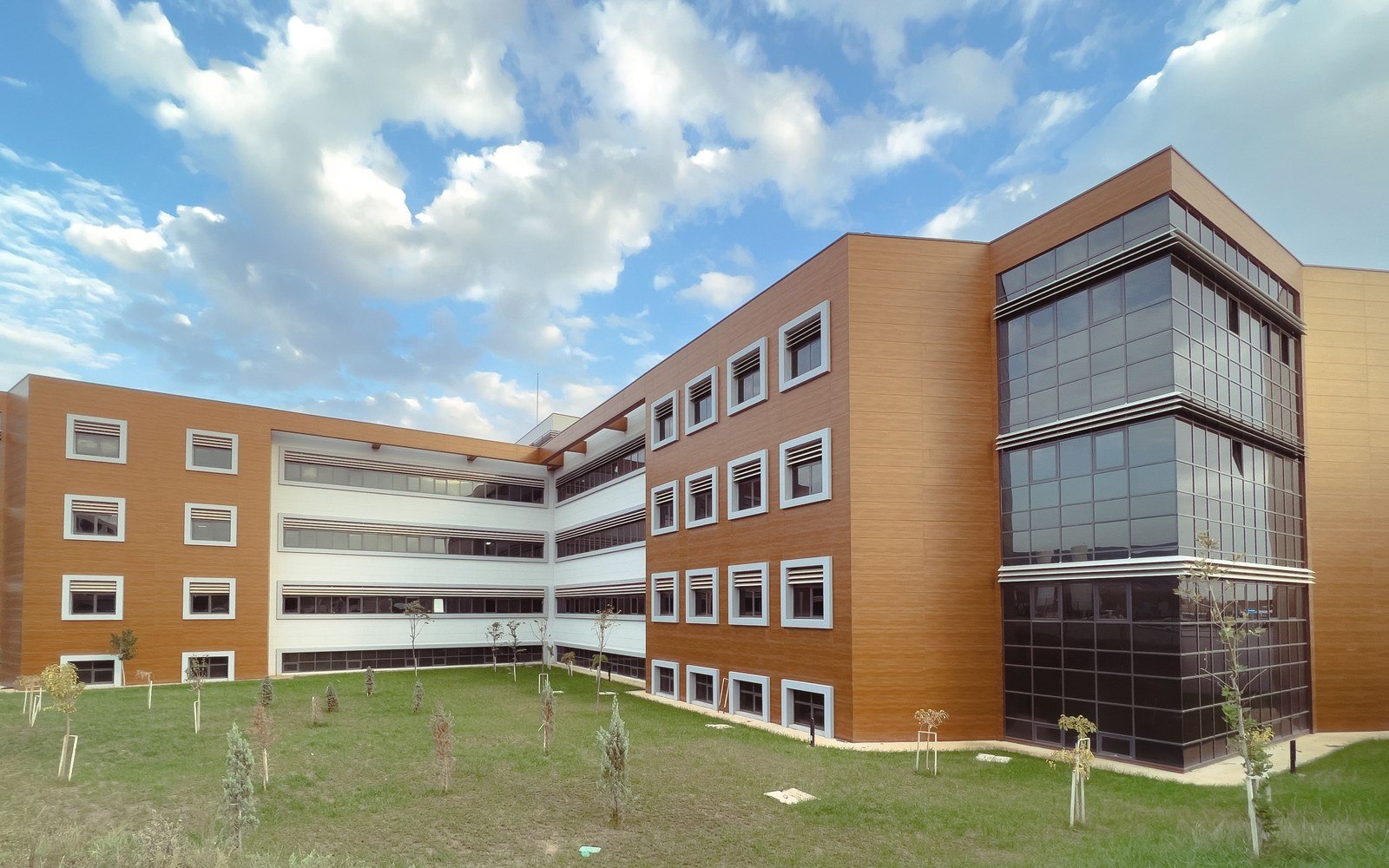 A modern multi storey educational building beside a grassed lawn under a cloudy sky