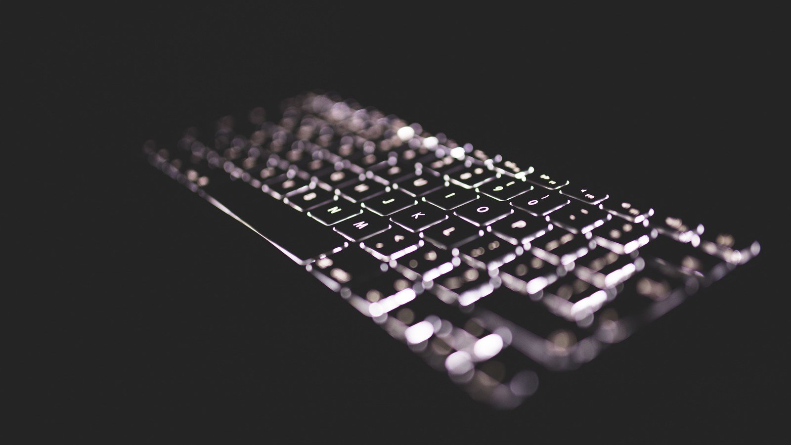A backlit computer keyboard glowing against a dark background