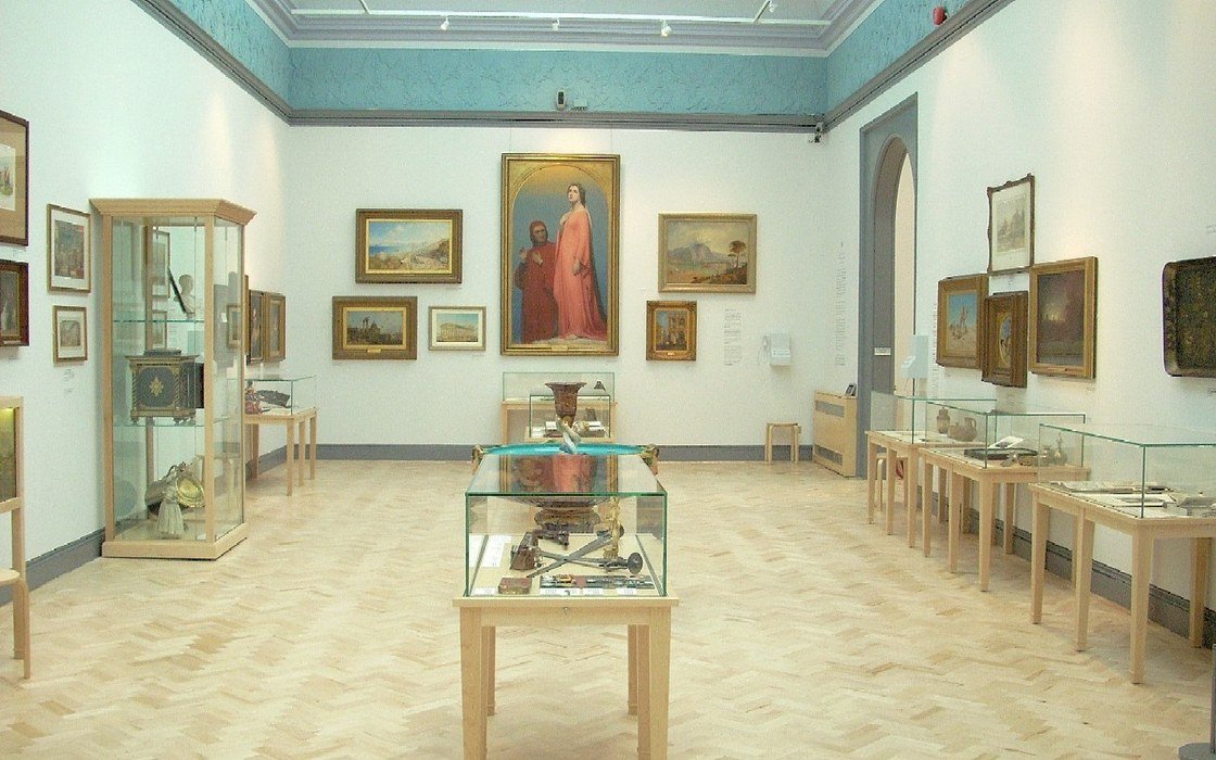 A gallery room with framed paintings on the walls and glass display cases on the floor