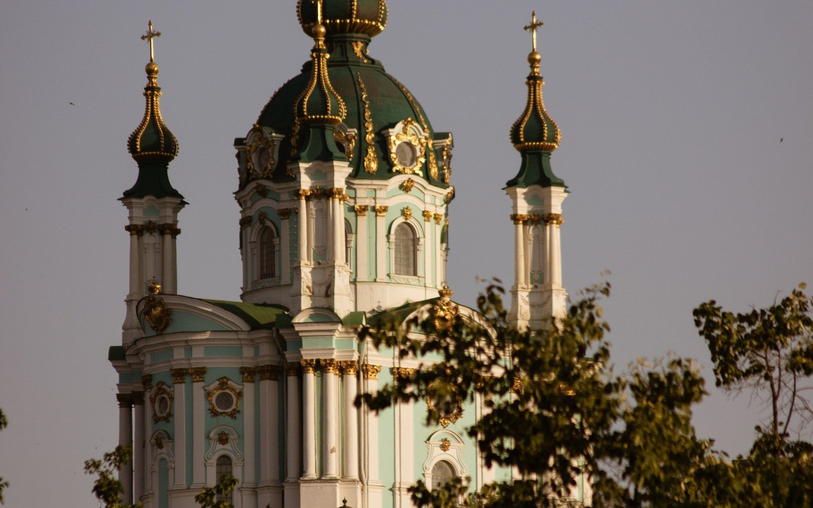 The green and gold baroque domes of Saint Andrew's Church in Kyiv at dusk