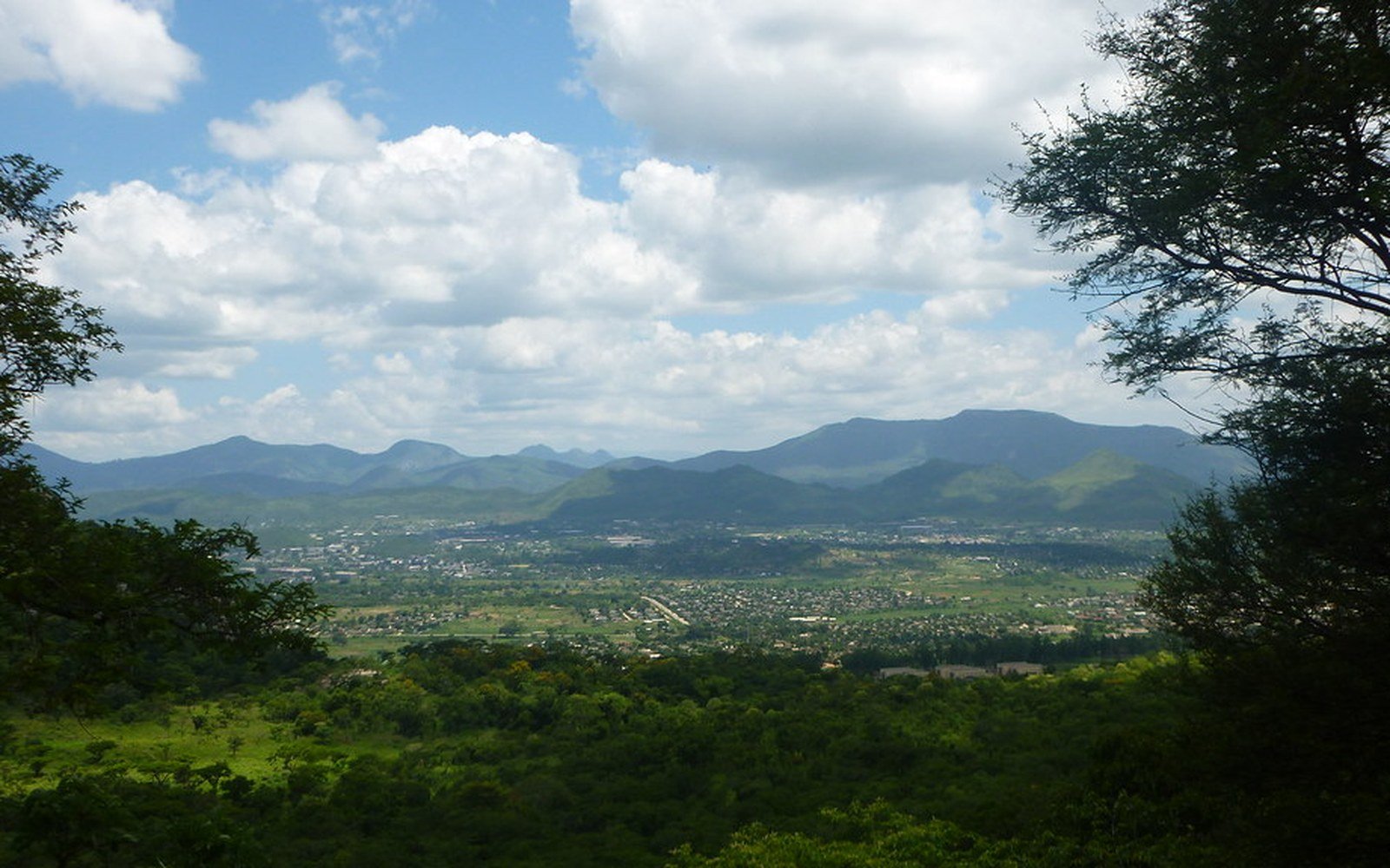 A wide green valley in Zimbabwe seen from a wooded ridge, with hills along the far horizon
