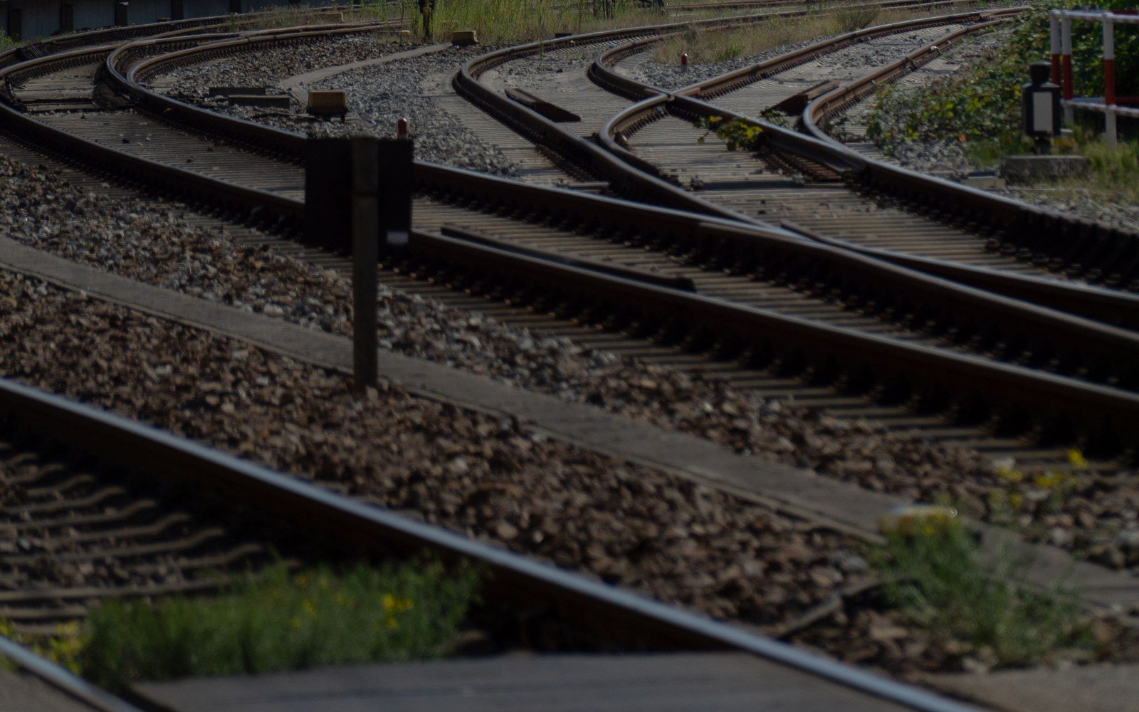 Several railway tracks curving away between ballast shoulders under a dense web of overhead line equipment and support masts