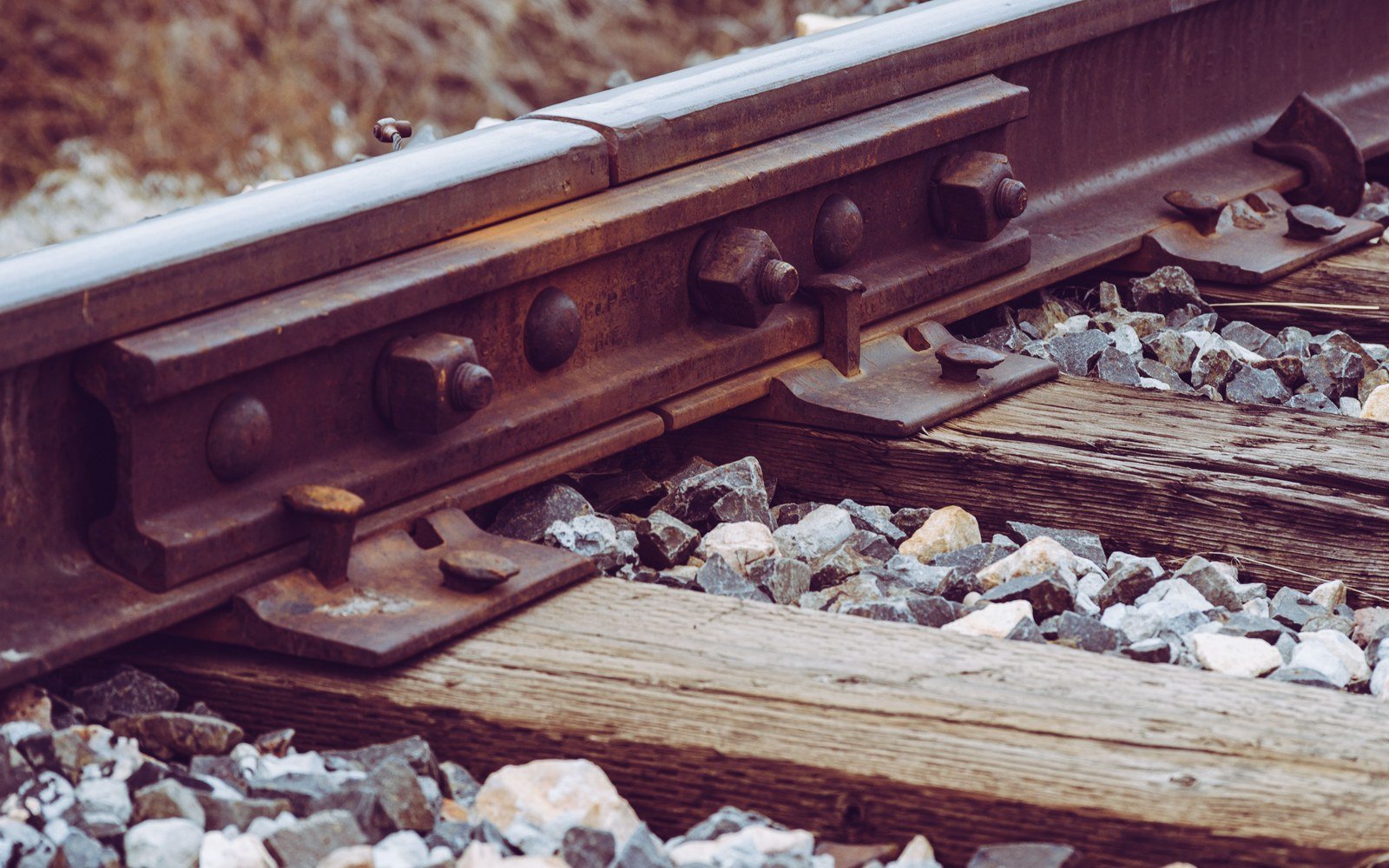 A close up of railway track, showing a rail bolted through a fishplate, a weathered timber sleeper and grey stone ballast
